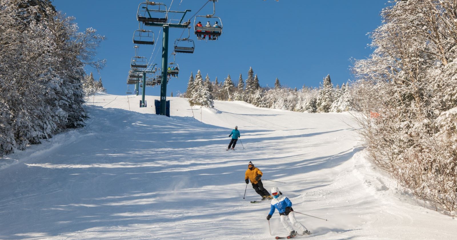 Three skiers on a slope, blue sky, above a chairlift.